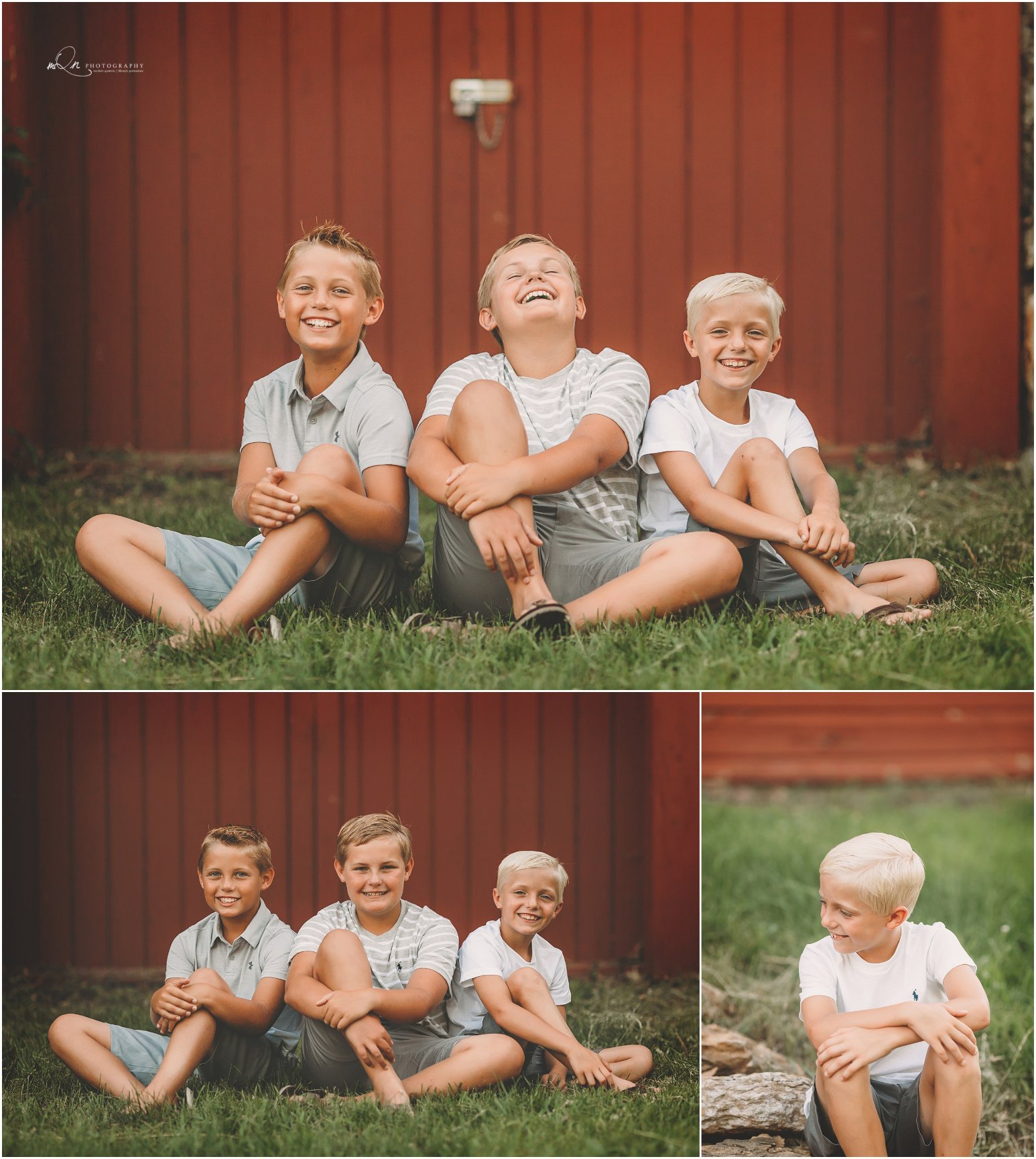 Three young children sitting on grass, smiling, in front of a red wooden wall. Casual summer outfits.