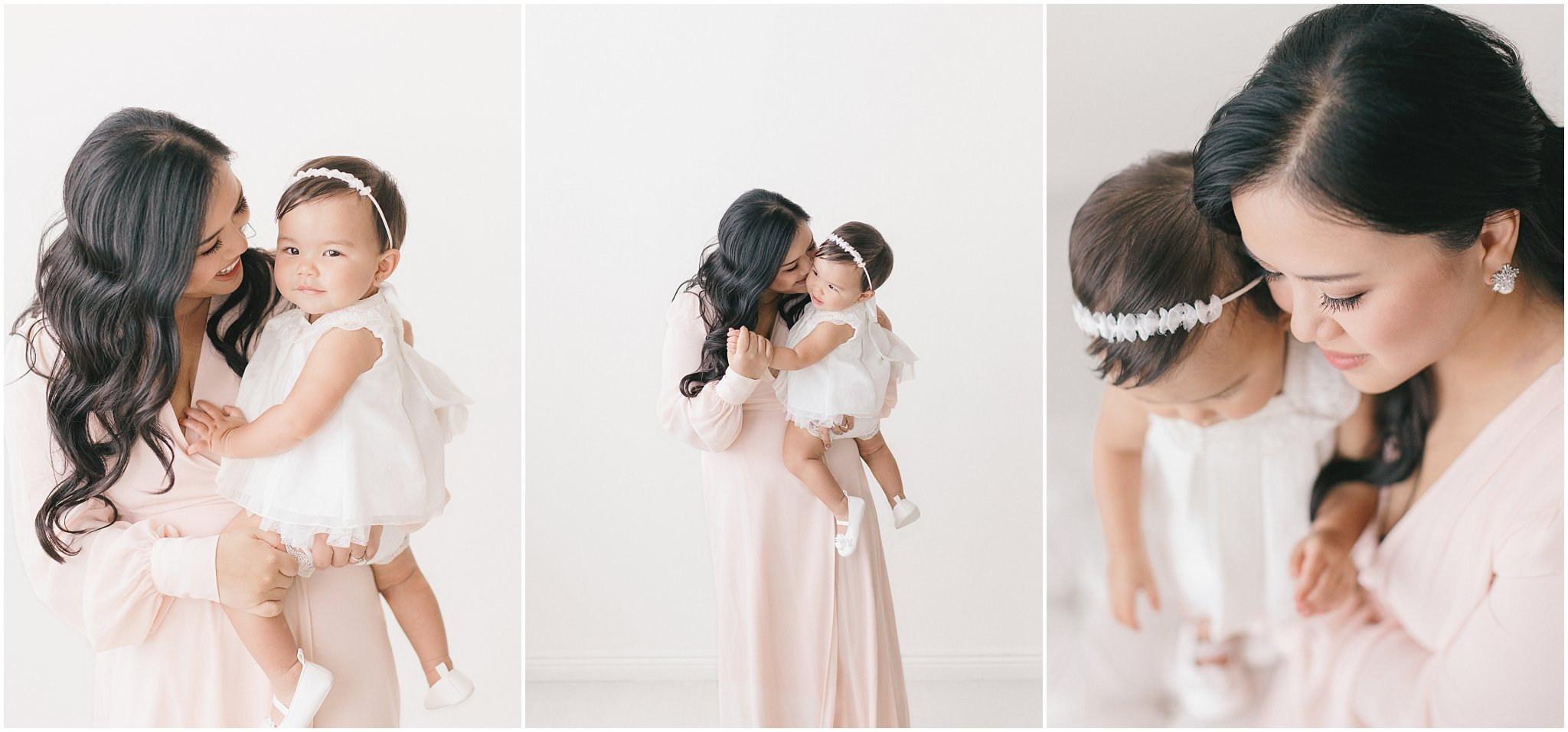 A mother holds her young daughter, both wearing elegant outfits, in a bright, minimalistic setting.