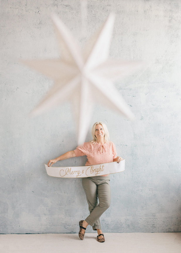Woman in casual clothing poses with a large star decoration against a textured wall.