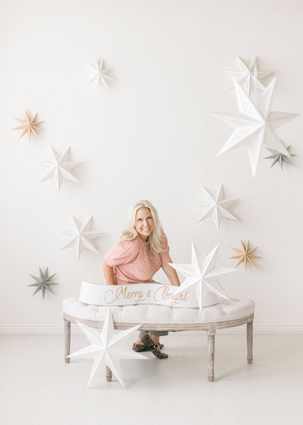 A woman in a pink top sits at a table with white decorative stars on a light background.