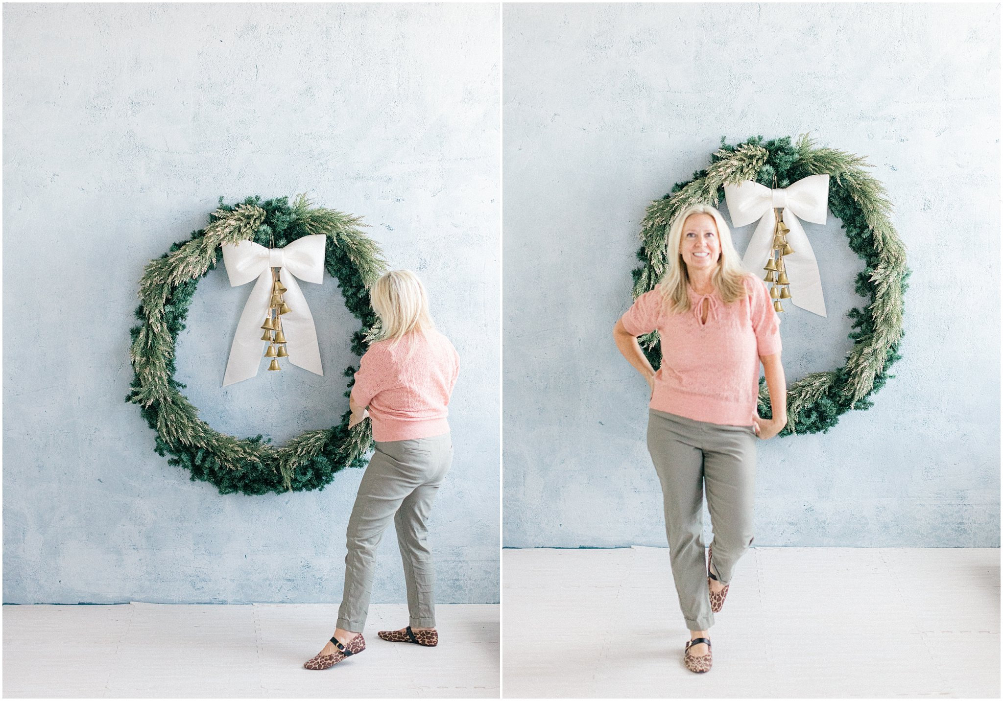 Woman in a pink top poses beside a large holiday wreath with a bow against a light blue background.
