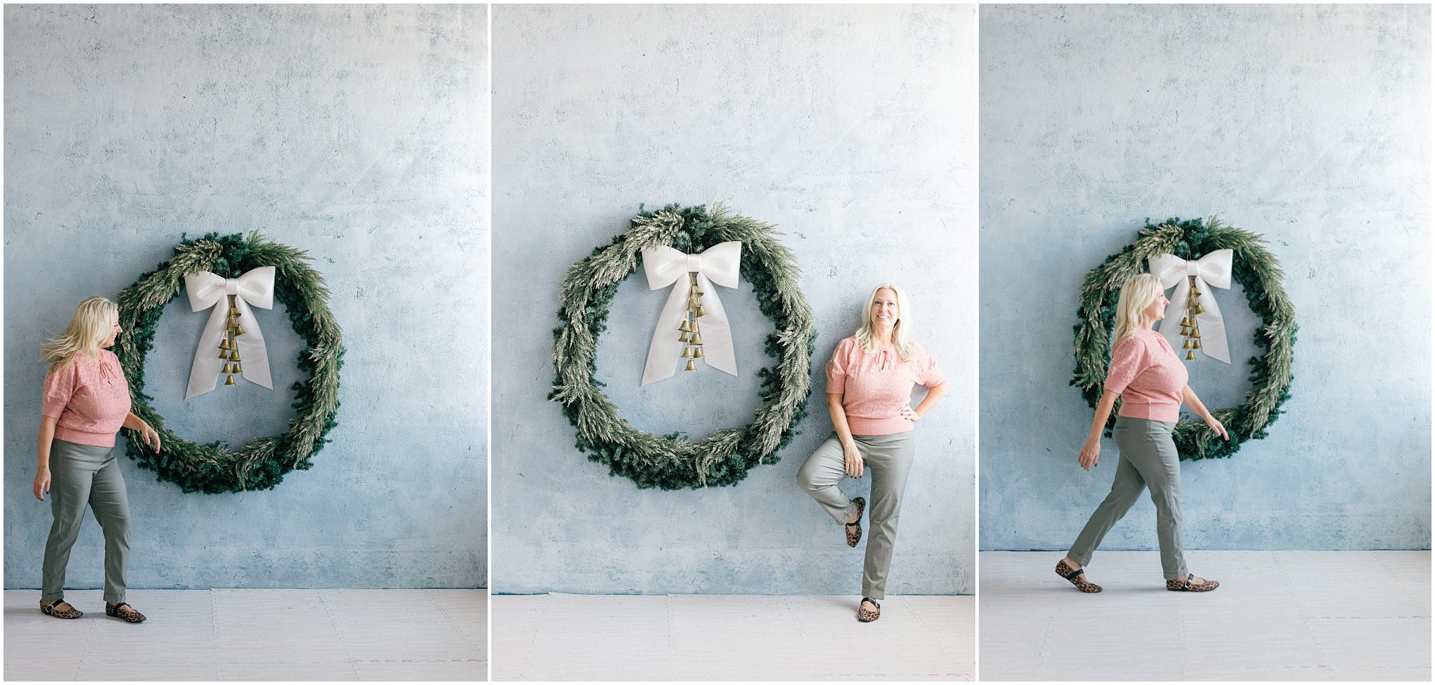 Woman in pink top poses beside a large decorative wreath on a light blue wall.