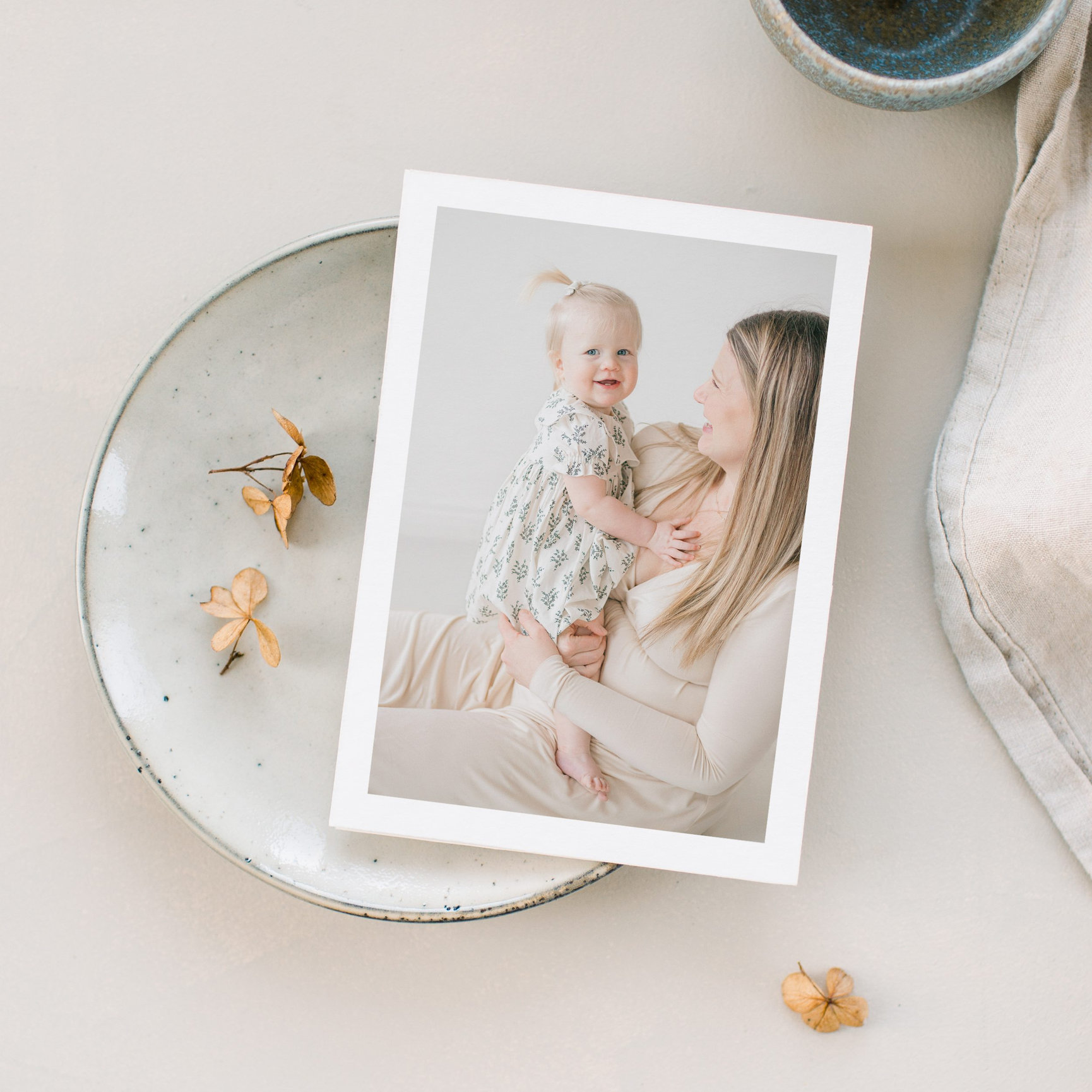 Framed photo of a mother holding a child, placed on a ceramic plate with dried flowers around.