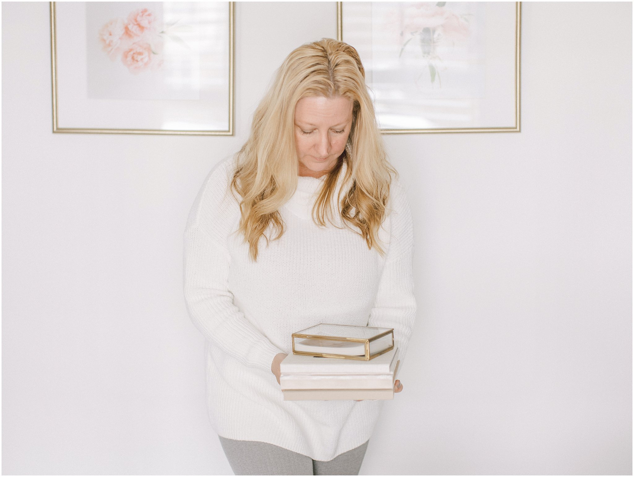 Woman in white sweater holding books, standing in a softly lit room.
