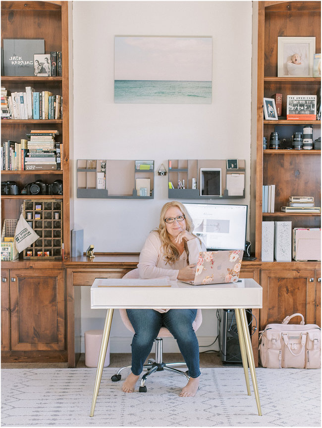 Person working at a desk in a home office with wooden shelves filled with books and decor.