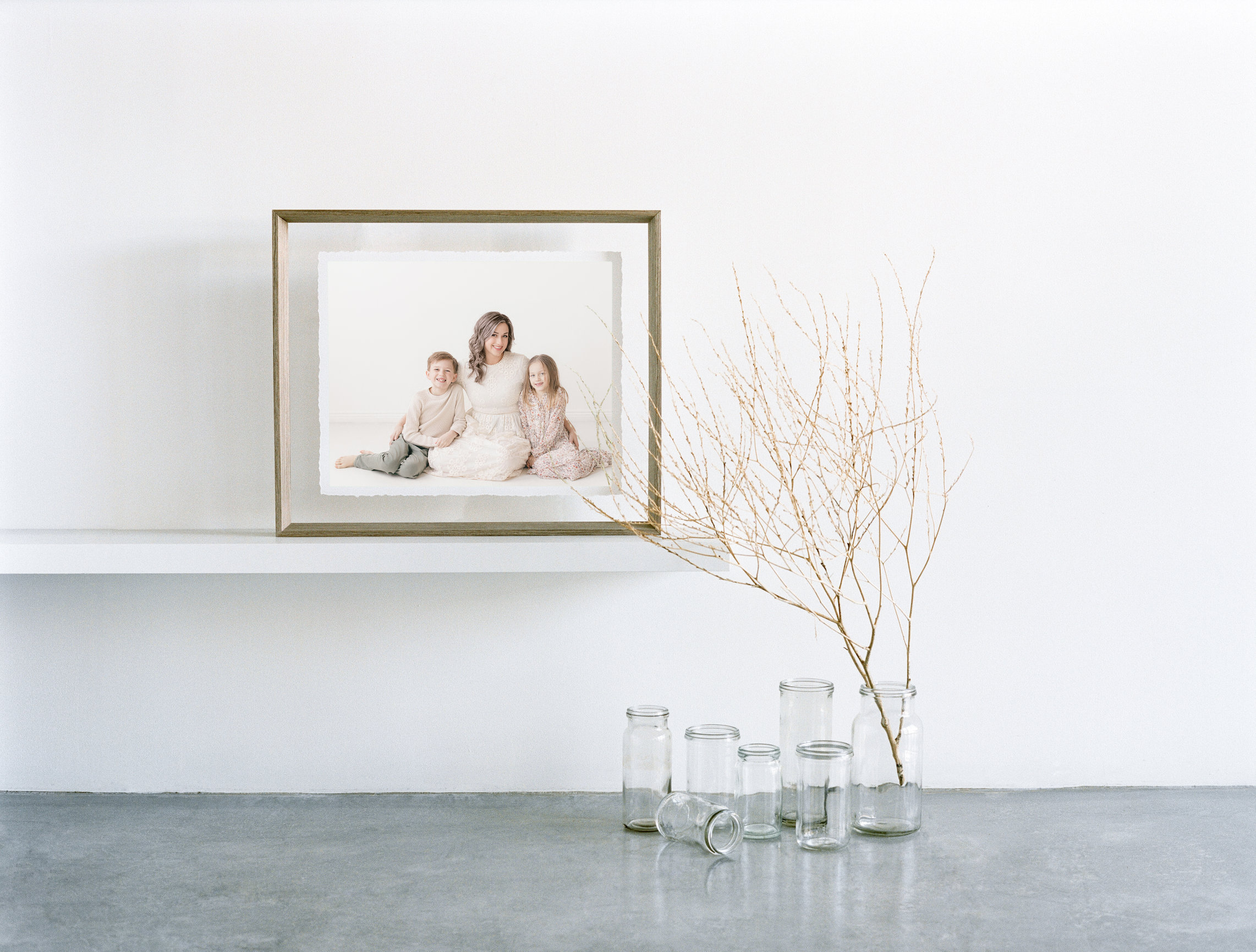 Framed family photo on a white shelf beside glass bottles and a bare branch.