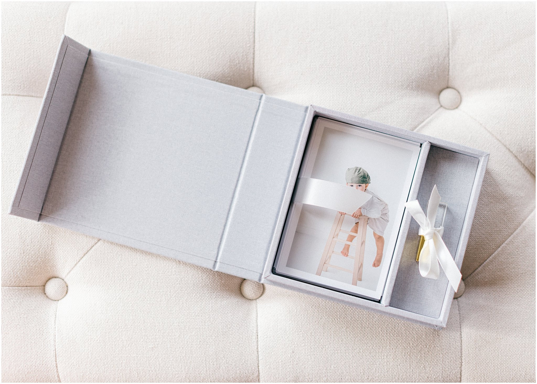 Gray gift box with sliding compartments containing a clear bottle and a folded item inside, placed on a cushioned surface.