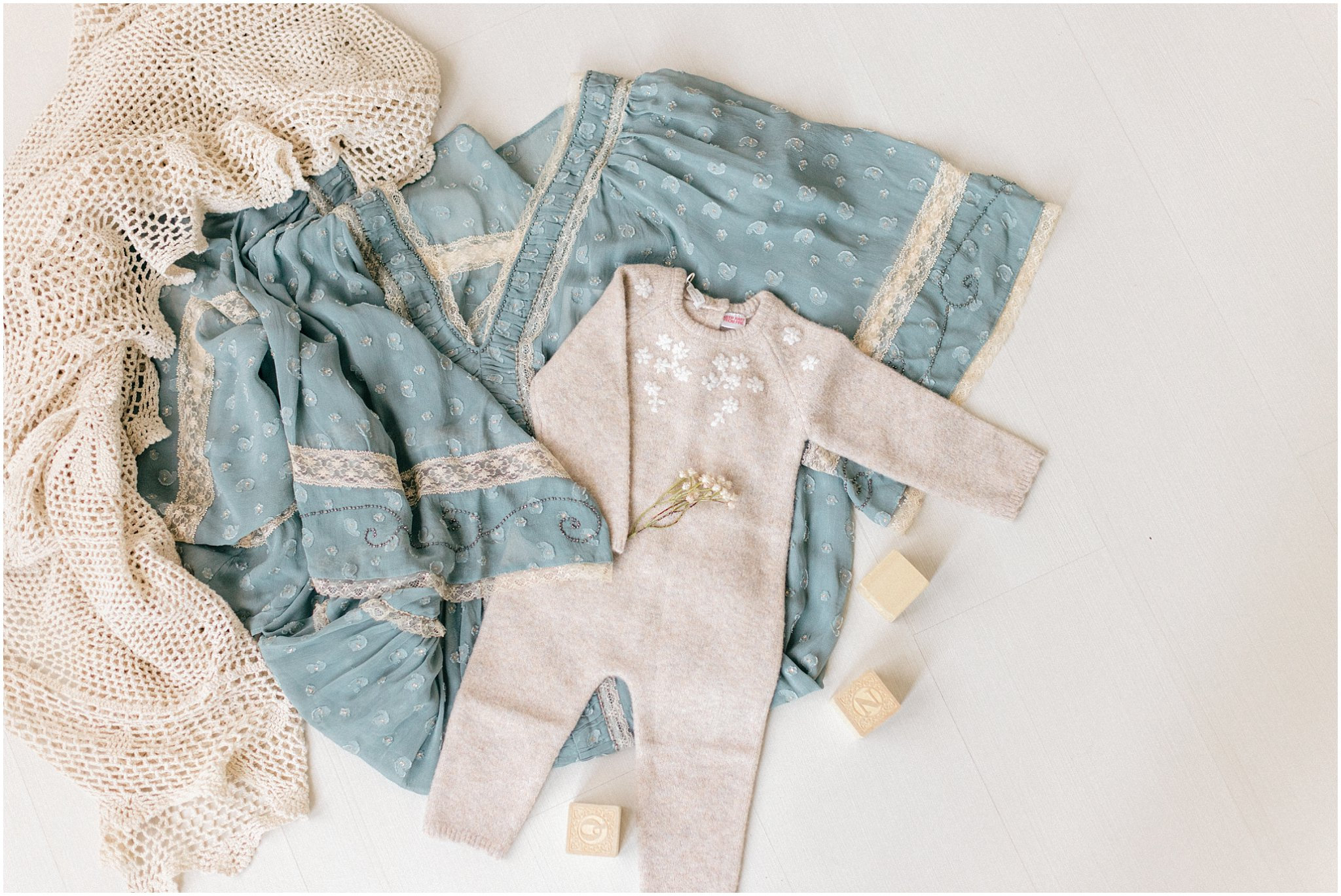 Baby outfit on a soft blue and white patterned fabric with decorative blocks nearby.