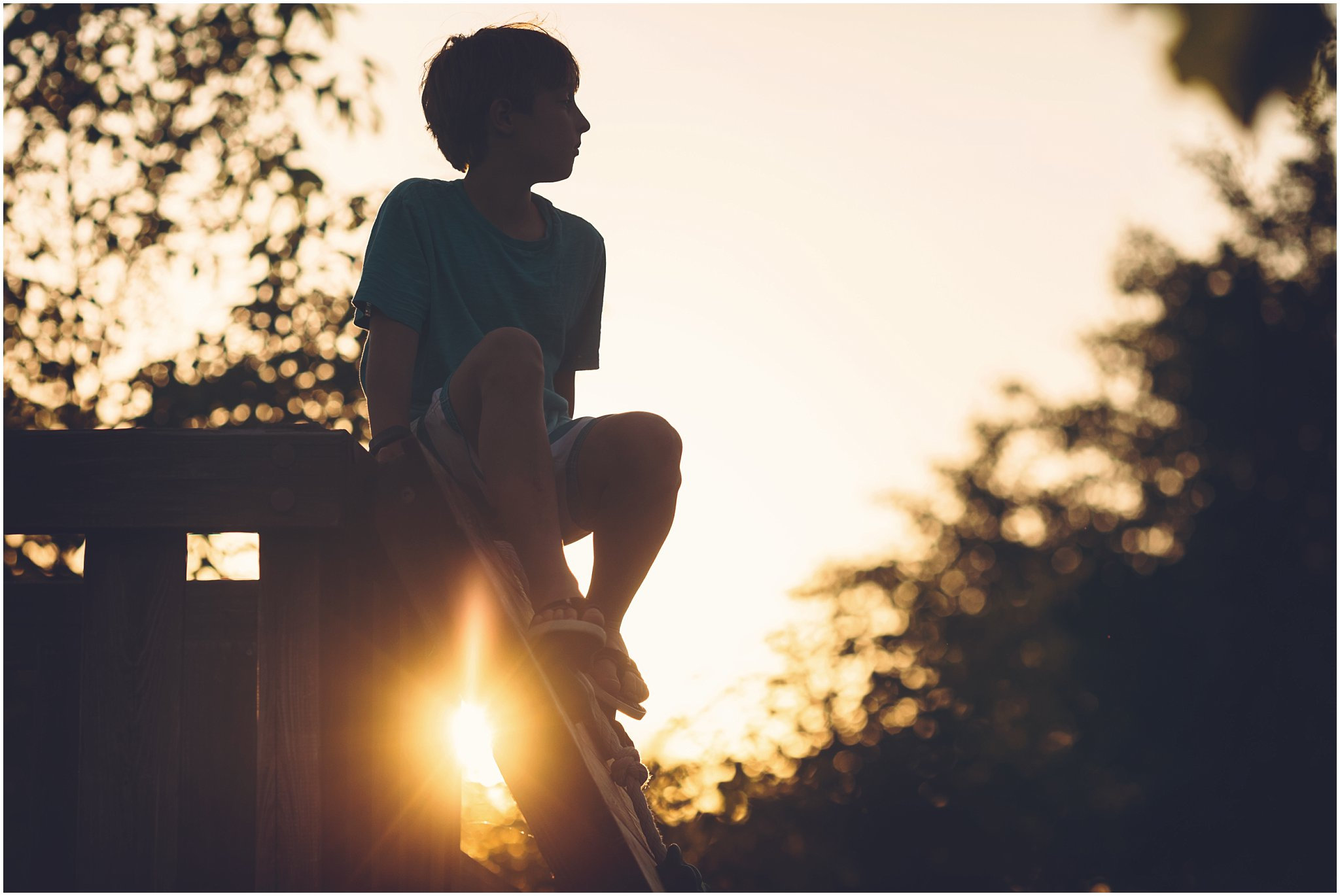 Silhouetted child sitting outdoors at sunset with trees in the background.