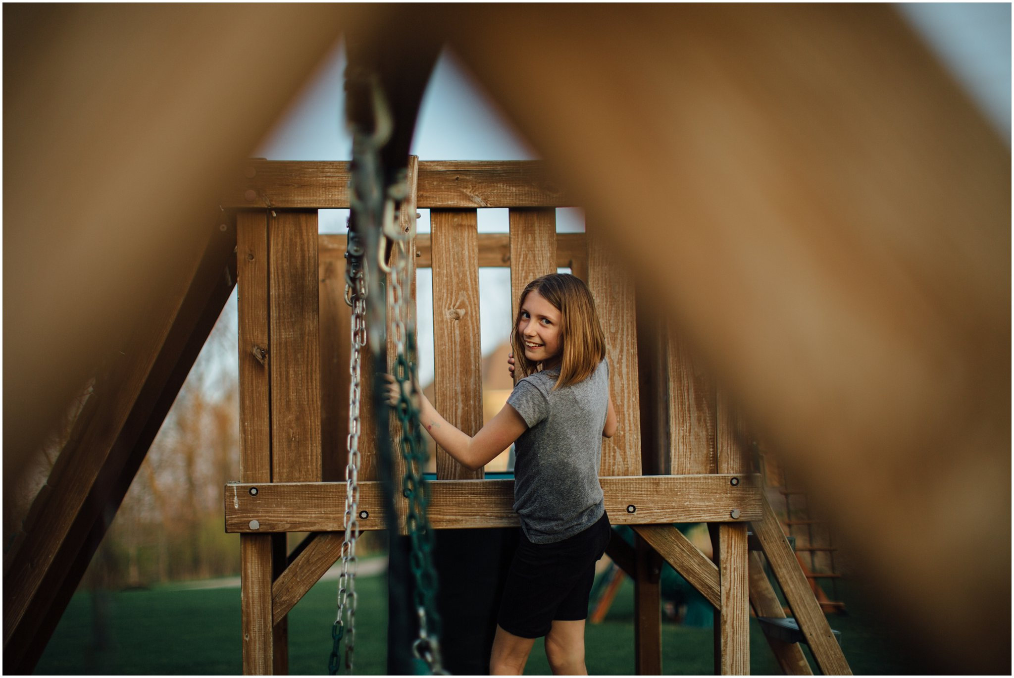 Child climbing a wooden play structure with a blurred foreground.