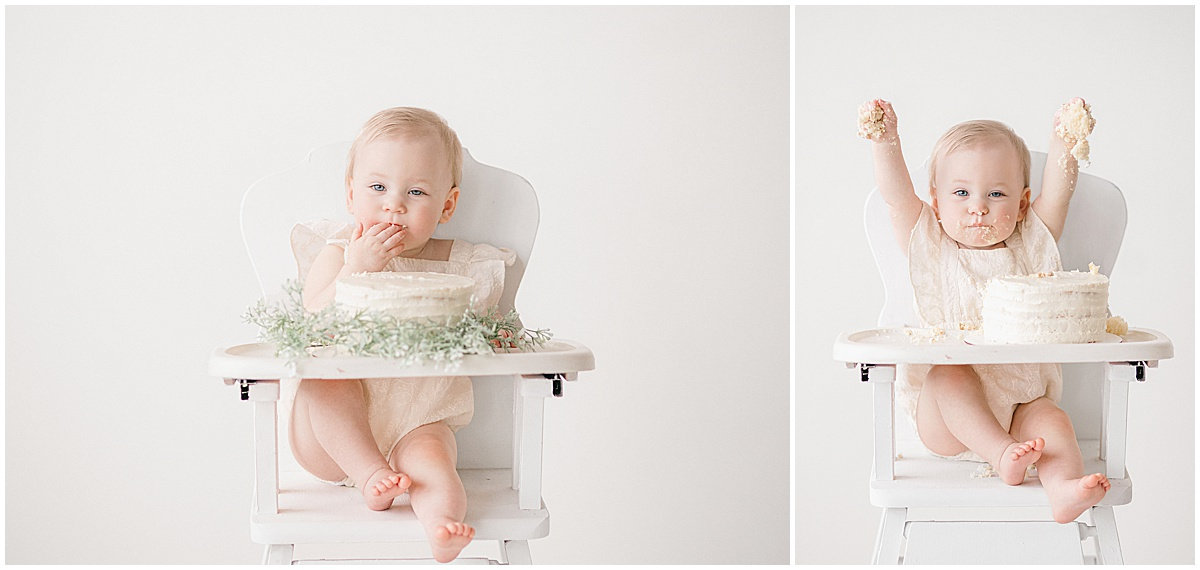 Baby sitting in a high chair with a cake, joyous expression, arms raised, celebrating a first birthday.