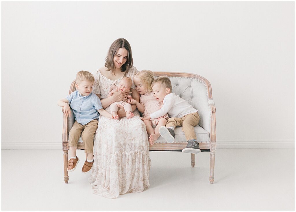 Minneapolis motherhood photographer capturing a mama snuggling her newborn while her three older children sit beside her in a bright studio