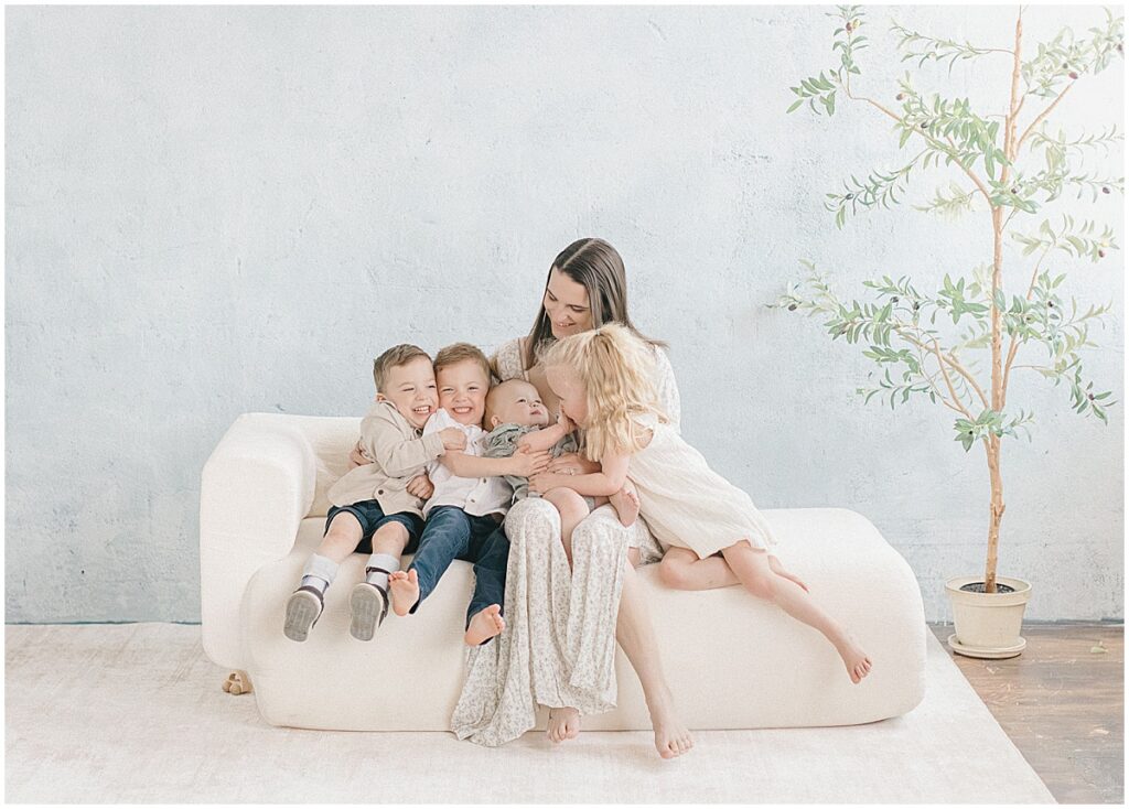 Minneapolis motherhood photographer capturing a mama with four children cuddled together on a white couch in a bright studio