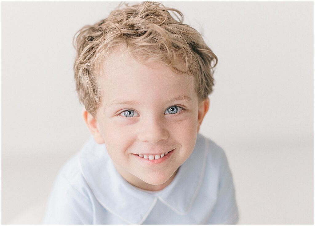 Close portrait of a smiling four-year-old boy looking up at the camera in a bright Minneapolis studio