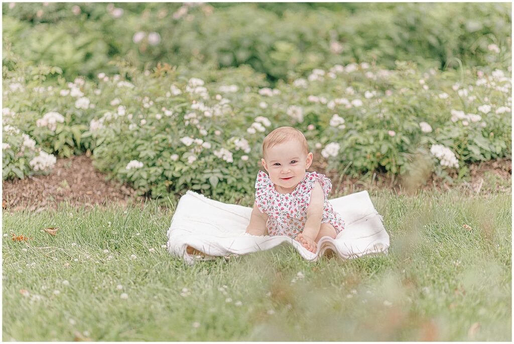 One year old baby girl smiling on a blanket during a first birthday photography session at the Lyndale Rose Garden in Minneapolis