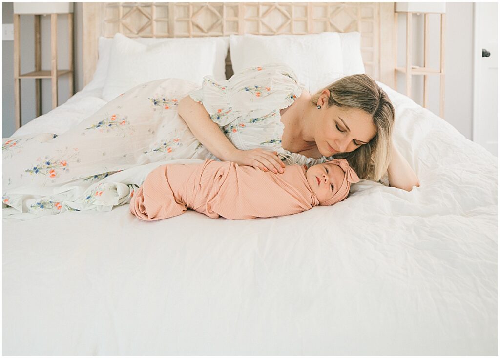 Mother lying beside her newborn baby on a bed during an in-home lifestyle newborn photography session in Minneapolis.