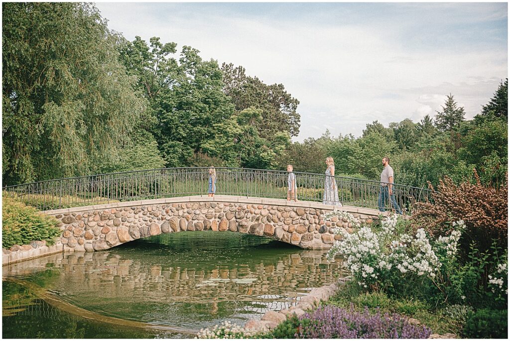 Family of four walking across a stone bridge in a lush garden in St. Paul's Como Park taken by St. Paul Photographer, Michele Quattrin of mQn Photography