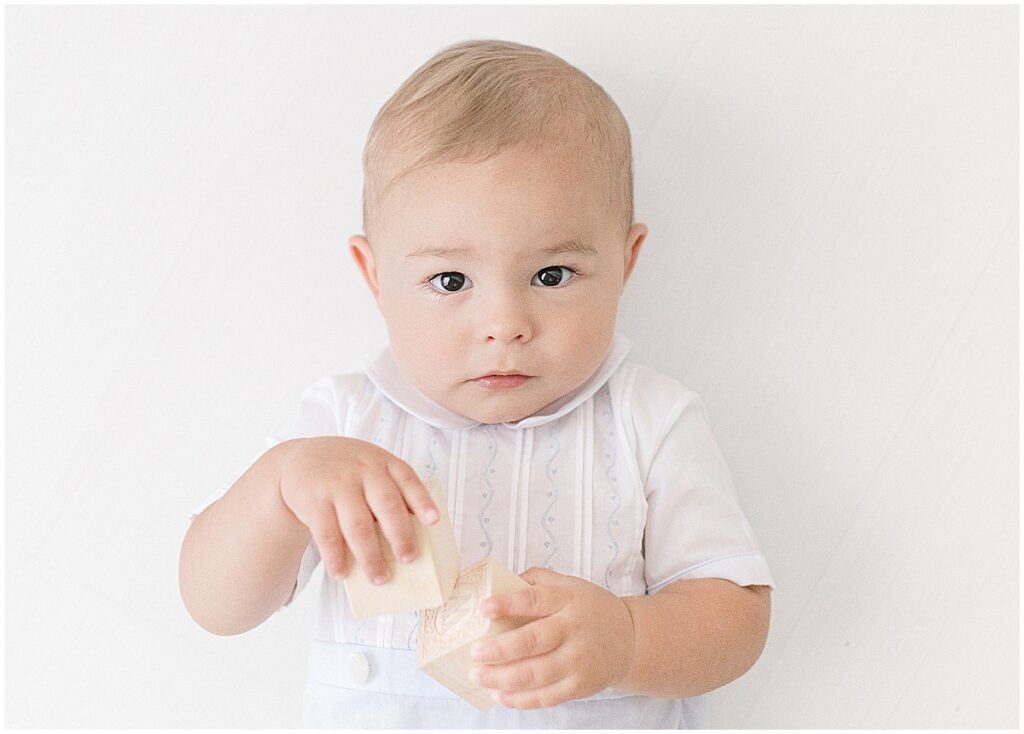 One-year-old baby holding wooden blocks during a 1 year milestone photos session in a Minneapolis studio.