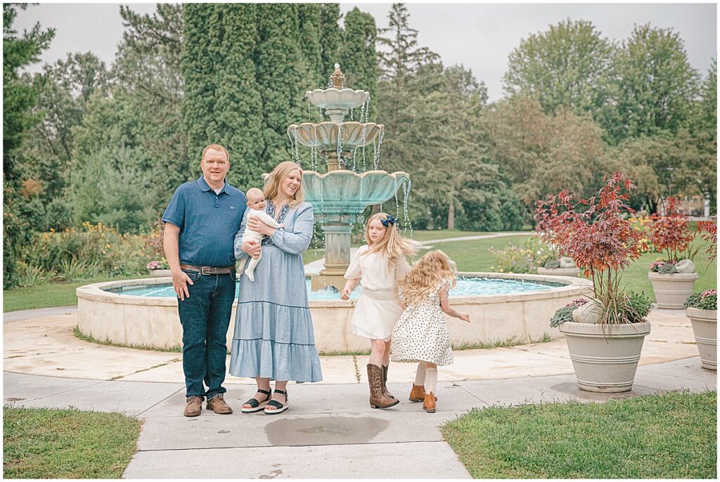 Arneson Acres family photos with two children dancing in front of the tiered garden fountain in Edina.