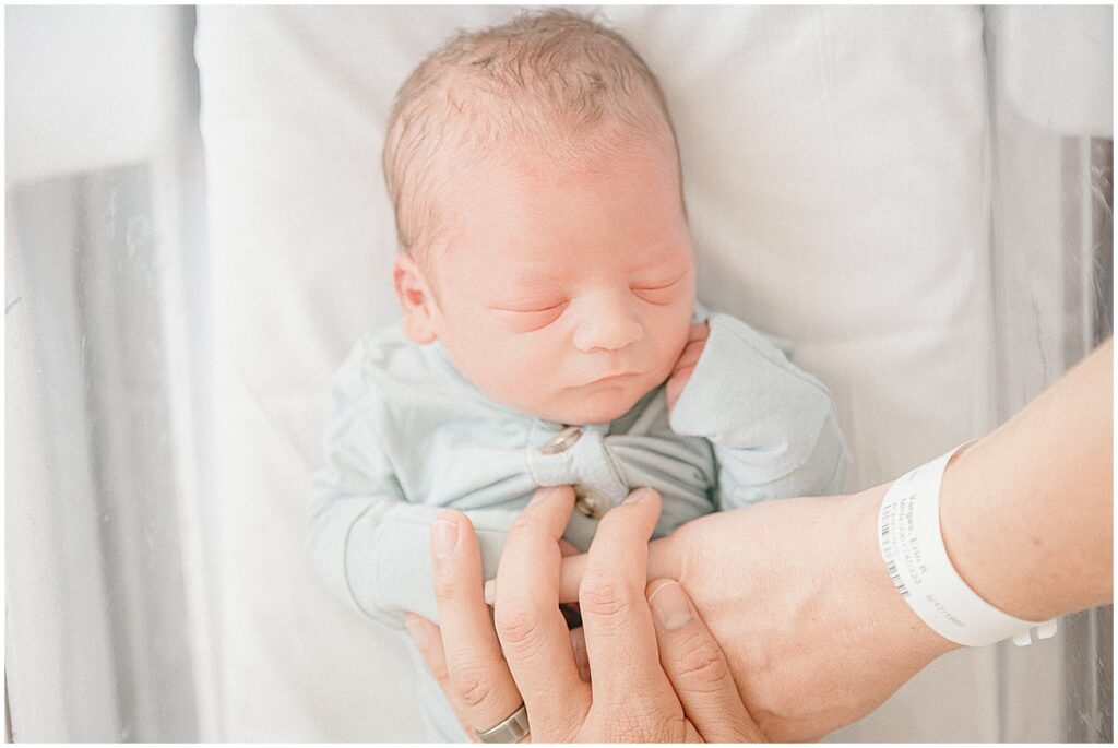 Fresh 48 hospital photography in Edina showing a newborn resting in a hospital bassinet with parents’ hands nearby.