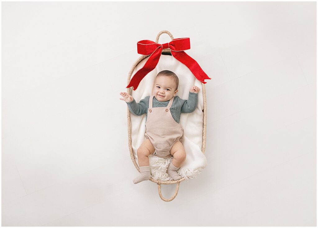 Baby smiling in a woven basket with a red velvet bow during a Minneapolis Christmas mini session.