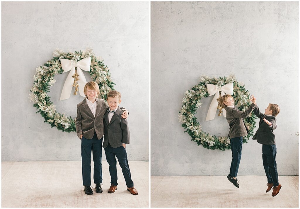 Two brothers in dress clothes posing and jumping in front of a holiday wreath during a Minneapolis Christmas mini session.