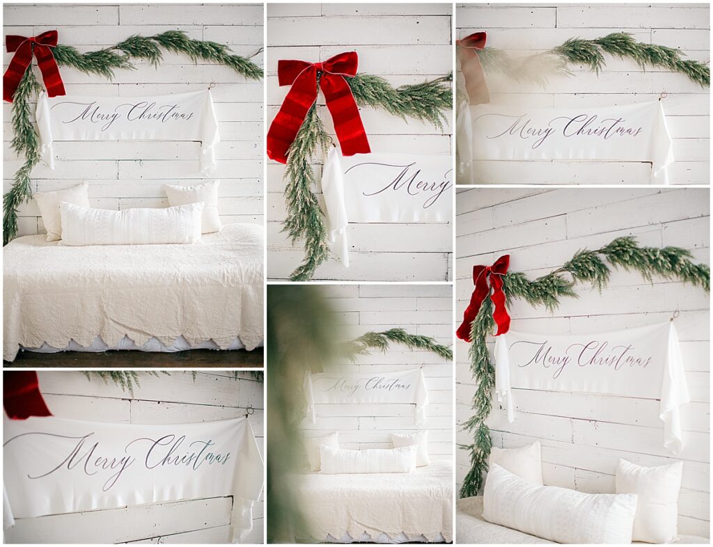 White Christmas bed set with greenery, red velvet bow, and Merry Christmas banner in a Minneapolis photography studio.