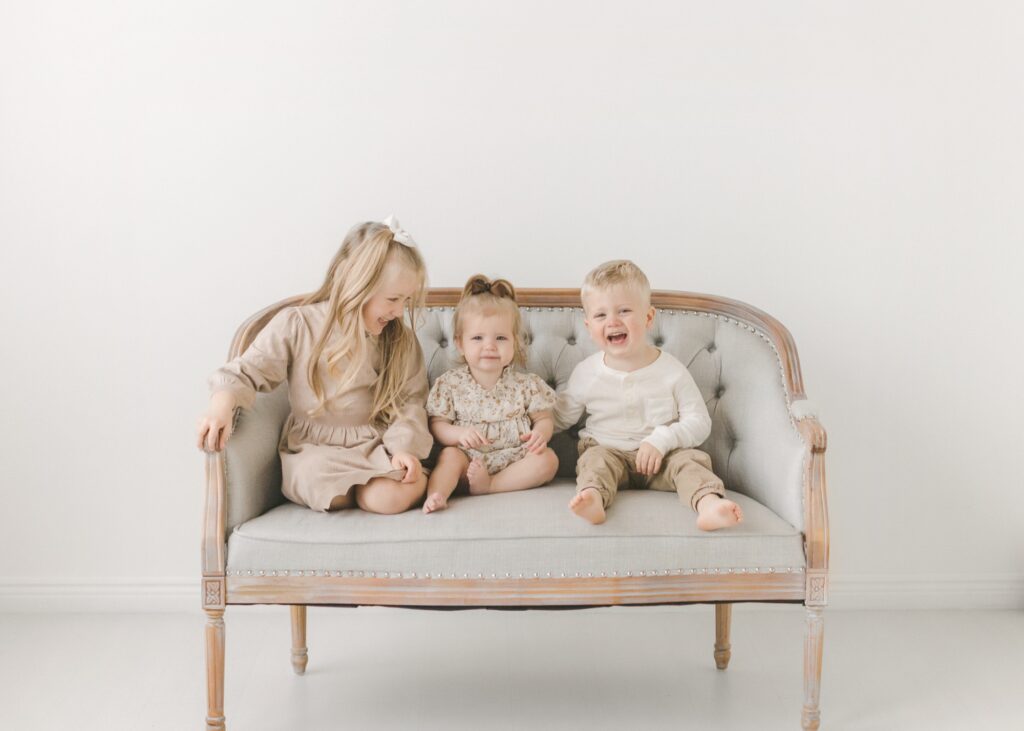Three siblings laughing on a settee in a white Minneapolis studio, a horizontal photo for a Christmas card