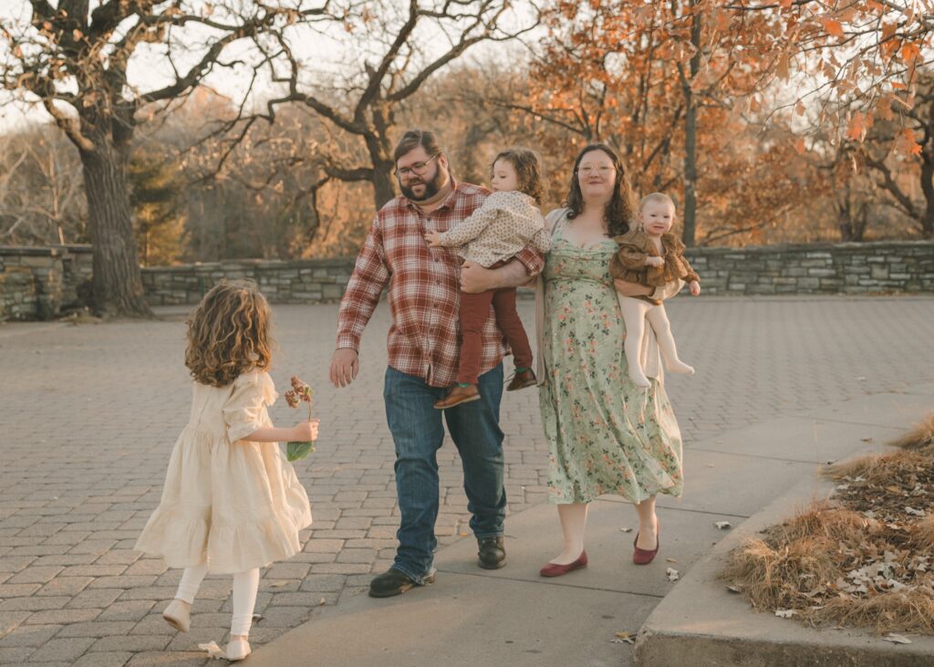 Christmas card photo ideas: family walking through a park in fall while their daughter runs ahead