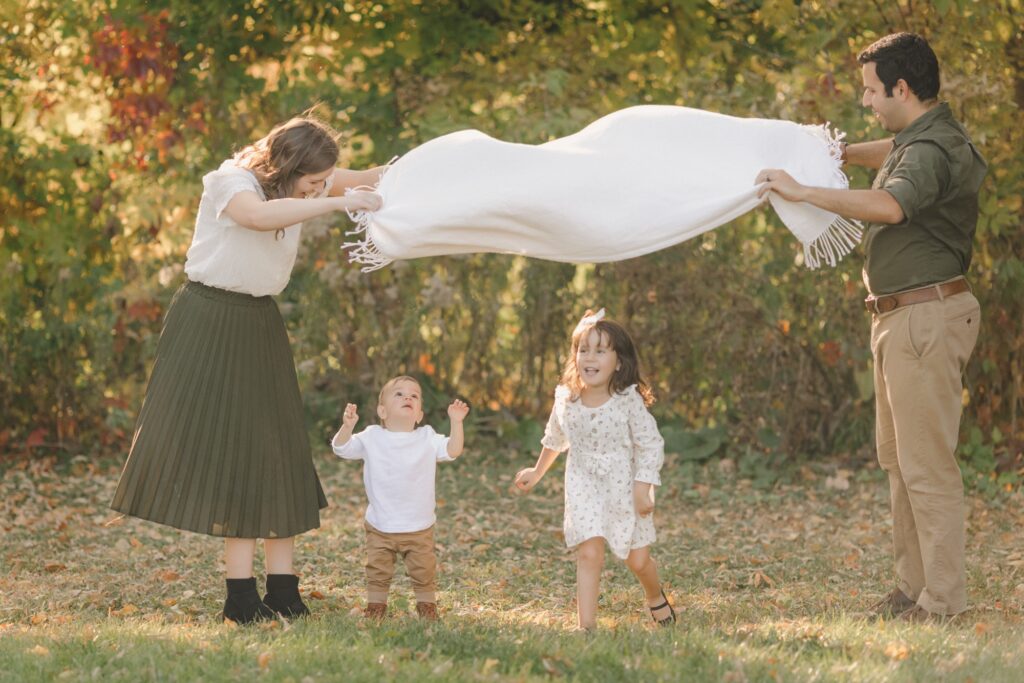 Family Christmas card photo ideas: parents swing a blanket over their laughing kids in a fall field